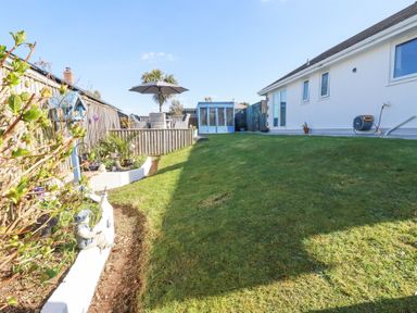 A garden with a lawn and patio furniture under an umbrella next to a white house at Palm View in Holywell Bay