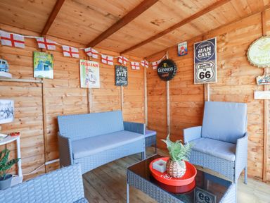 A wooden room with wicker sofa and chairs and vintage signs on the walls at Palm View in Holywell Bay