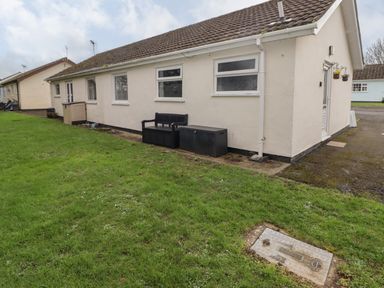 The exterior of a single-story cream colored house with a lawn bench and storage box on the side at 13 Gower Holiday Village in Scurlage
