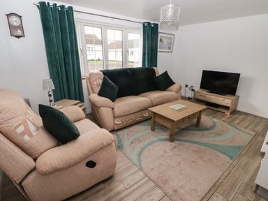 A living room with beige sofas green cushions a coffee table and a television at 13 Gower Holiday Village in Scurlage