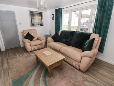 A living room with beige sofas green cushions wooden coffee table and large windows with green curtains at 13 Gower Holiday Village in Scurlage