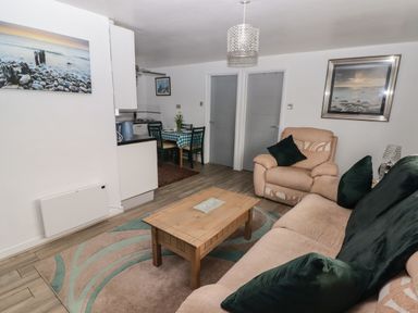 A living room with a sofa and armchair around a wooden coffee table and a dining area with a table and chairs at 13 Gower Holiday Village in Scurlage