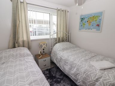 A bedroom with two single beds a nightstand with a lamp and clock a window with curtains and a world map on the wall at 13 Gower Holiday Village in Scurlage