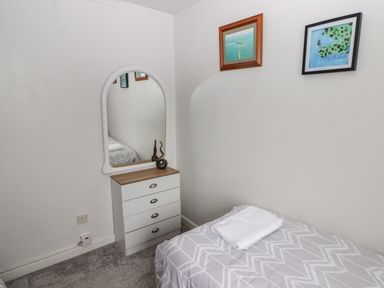 A small bedroom with a single bed covered in patterned bedding and a folded towel on top a chest of drawers with a mirror above it and two framed pictures on the wall at 13 Gower Holiday Village in Scurlage