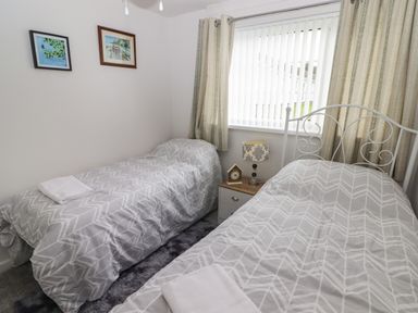 A bedroom with two single beds a nightstand with a lamp and clock and framed pictures on the wall at 13 Gower Holiday Village in Scurlage