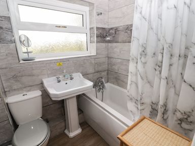 A bathroom with a toilet sink bathtub and marble patterned shower curtain at 13 Gower Holiday Village in Scurlage