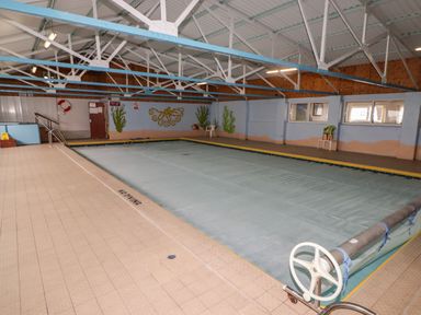 An indoor swimming pool with a cover over the water and marine-themed wall paintings at 13 Gower Holiday Village in Scurlage