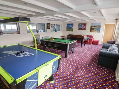 A game room with air hockey, pool table, foosball table, chairs, and sofas at 13 Gower Holiday Village in Scurlage