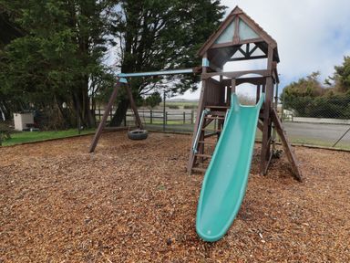 A playground with a green slide wooden climbing structure swing tire and wood chip ground at 13 Gower Holiday Village in Scurlage