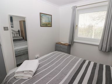 A bedroom with a bed striped gray and white a mirror dresser and window with gray curtains at 13 Gower Holiday Village in Scurlage