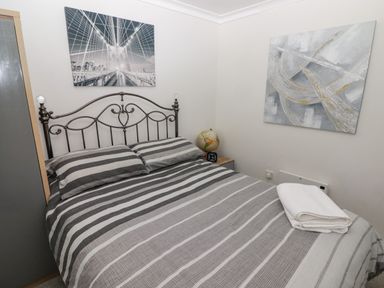 A bedroom with a double bed striped bedding a bedside table with a globe and clock and two paintings on the wall at 13 Gower Holiday Village in Scurlage