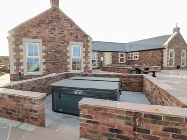 An outdoor hot tub surrounded by brick walls with a brick house and picnic table in the background at Glebe Cottage in Embleton