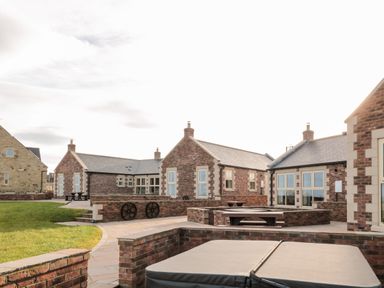 A courtyard with brick buildings and picnic tables at Glebe Cottage in Embleton