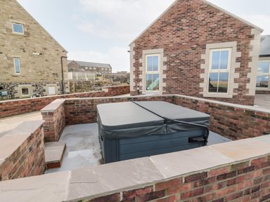 A covered hot tub in a brick-walled outdoor area with buildings in the background at Glebe Cottage in Embleton