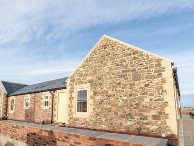 An exterior view of a stone and brick building with a yellow door and windows behind a brick wall at Glebe Cottage in Embleton