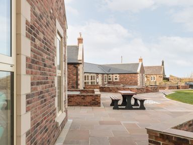 An outdoor paved area with benches and tables next to brick buildings at Glebe Cottage in Embleton