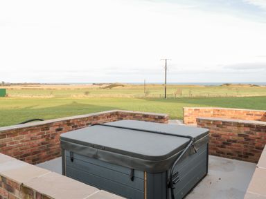 A covered hot tub surrounded by brick walls with green fields and an ocean in the background at Glebe Cottage in Embleton