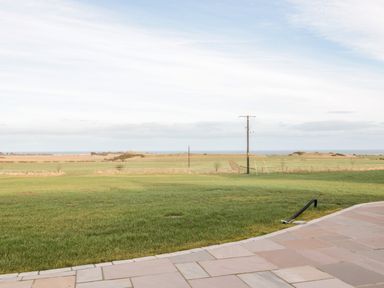 A view of a grassy field with telephone poles and a tiled patio in the foreground at Glebe Cottage in Embleton