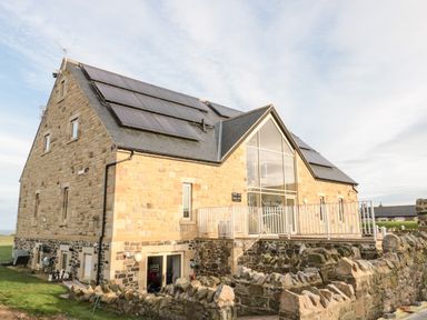 A stone building with solar panels on the roof and a glass entrance at Glebe Cottage in Embleton