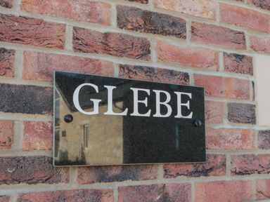 A black rectangular sign with white letters spelling glebe mounted on a brick wall at Glebe Cottage in Embleton