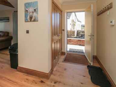 An entryway with an open door leading outside a wooden closet a wall coat rack and a painting of a cow at Glebe Cottage in Embleton