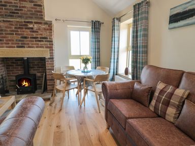 A living room with a brick fireplace wooden table with chairs and brown leather sofas at Glebe Cottage in Embleton