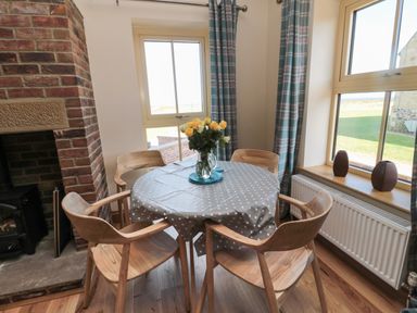 A dining area with a round table covered by a polka dot tablecloth surrounded by wooden chairs and a brick fireplace at Glebe Cottage in Embleton