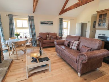 A living room with two brown sofas, a wooden coffee table, and a dining table with four chairs at Glebe Cottage in Embleton