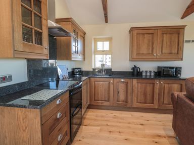A kitchen with wooden cabinets black countertops a stove microwave and a window at Glebe Cottage in Embleton