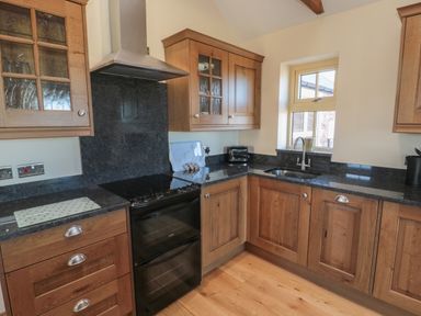 A kitchen with wooden cabinets black countertop sink and stove at Glebe Cottage in Embleton