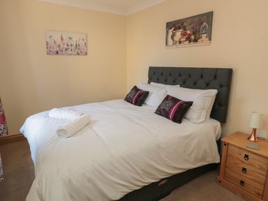 A bedroom with a double bed white bedding pillows and rolled towels next to a wooden bedside table with a lamp at Glebe Cottage in Embleton