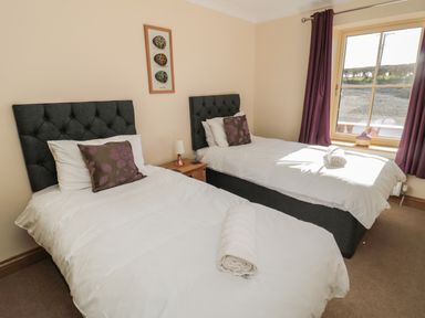 A bedroom with two single beds a window with curtains and a nightstand at Glebe Cottage in Embleton