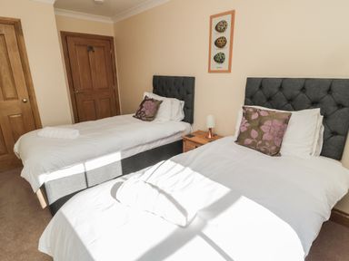 A bedroom with two single beds a nightstand between them and wooden doors at Glebe Cottage in Embleton