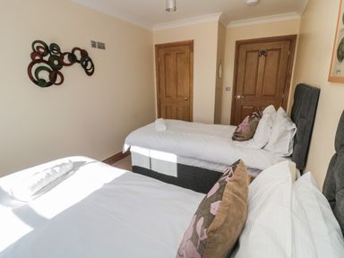 A bedroom with two single beds white bedding wooden doors and wall art at Glebe Cottage in Embleton