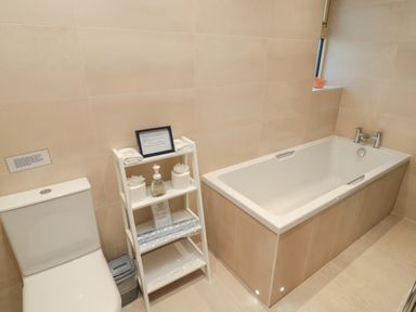 A bathroom with a toilet a bathtub a small shelving unit with towels and toiletries at Glebe Cottage in Embleton