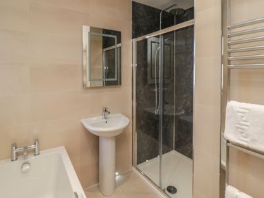 A bathroom with a bathtub sink shower enclosure and heated towel rail at Glebe Cottage in Embleton