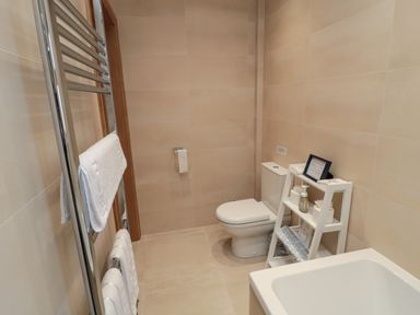 A bathroom with a toilet a towel rack with white towels and a shelf with toiletries at Glebe Cottage in Embleton