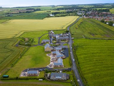 An aerial view of a rural area with multiple buildings surrounded by green fields and a nearby village at Glebe Cottage in Embleton
