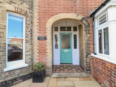 An arched entrance with a turquoise door and tiled floor at Collett House in Southwold