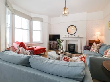 A living room with two blue sofas a red armchair a fireplace a television and a window at Collett House in Southwold