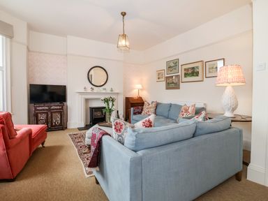 A living room with a blue sectional sofa red armchair television on cabinet fireplace and framed paintings at Collett House in Southwold