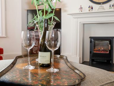 A bottle of wine and glasses on a tray in front of a fireplace and a television at Collett House in Southwold