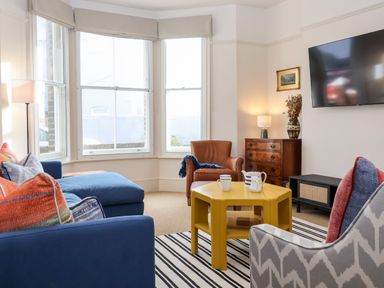 A living room with blue sofa orange and blue pillows a leather chair yellow coffee table and a wall mounted tv at Collett House in Southwold