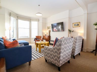 A living room with armchairs a blue sofa a yellow coffee table and a wall mounted television at Collett House in Southwold