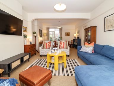 A living room with blue sofa, armchairs with patterned cushions, yellow coffee table and television on the wall at Collett House in Southwold