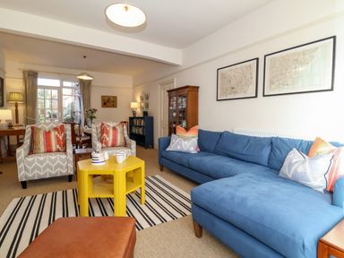 A living room with a blue sectional sofa two patterned armchairs a yellow coffee table and a striped rug at Collett House in Southwold