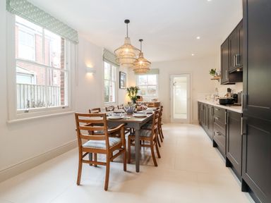 A kitchen with a dining table and wooden chairs next to dark cabinets at Collett House in Southwold