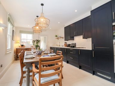 A kitchen with black cabinets a wooden dining table with chairs and pendant lights at Collett House in Southwold