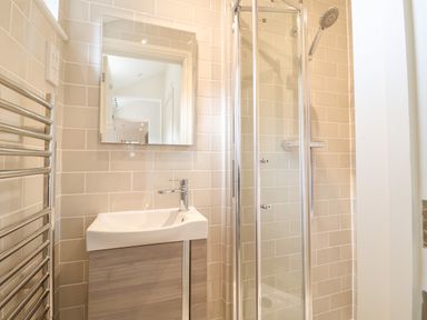 A bathroom with a sink cabinet mirror heated towel rail and a glass shower enclosure at Collett House Southwold