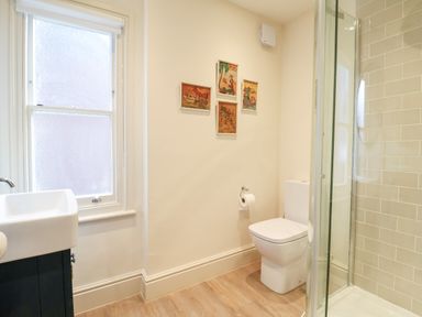 A bathroom with a toilet sink window shower and four framed pictures on the wall at Collett House in Southwold